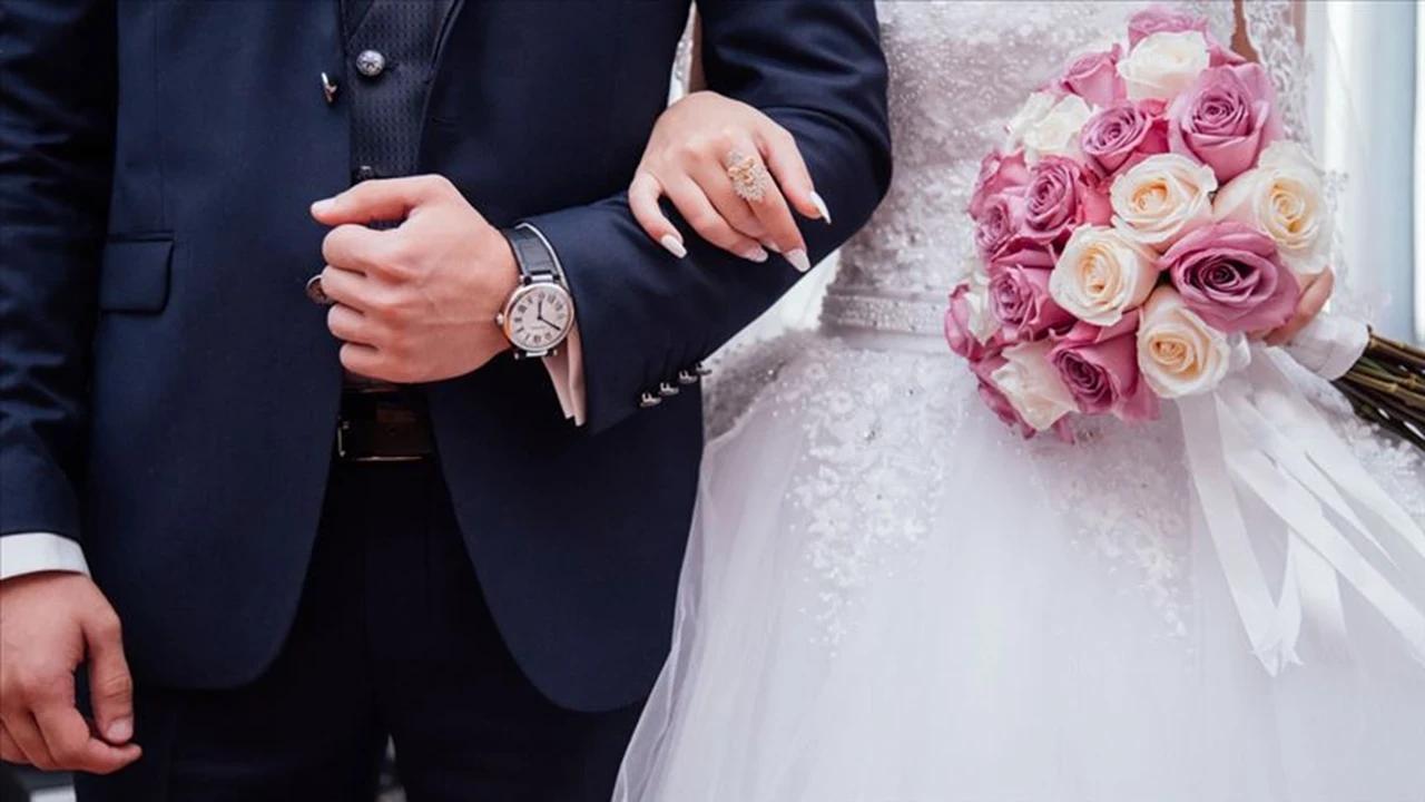 Damat ve gelinin kolları, gelinin elindeki yüzük ve pembe-beyaz çiçek buketiyle birlikte görülüyor.