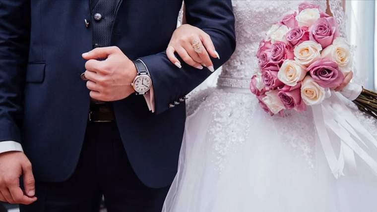 Damat ve gelinin kolları, gelinin elindeki yüzük ve pembe-beyaz çiçek buketiyle birlikte görülüyor.