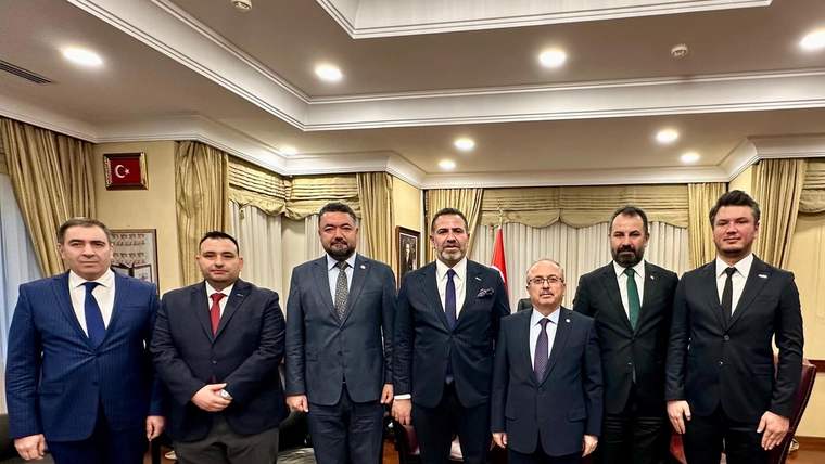 Türk bayrağının bulunduğu salonda, takım elbiseli yedi erkek yan yana poz veriyor.