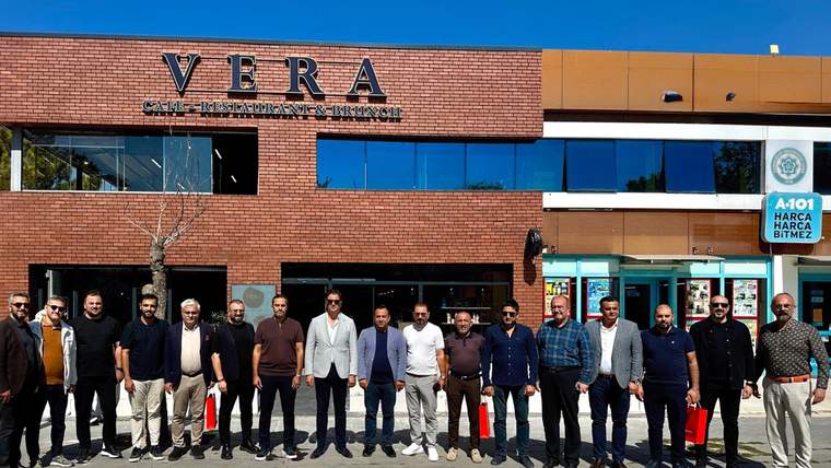 Üzerinde VERA yazan binanın önünde, kaldırımda yan yana duran bir grup insan görülüyor.