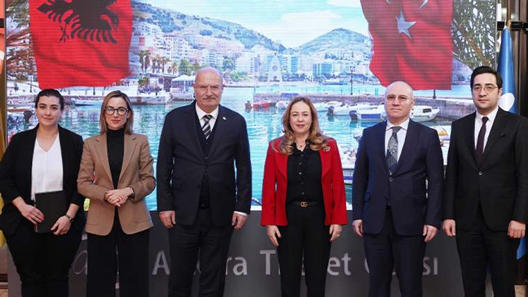 Arnavutluk ve Türkiye bayrakları önünde, şehir manzaralı fonda yan yana duran altı kişi