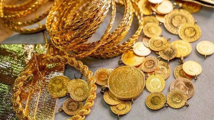 Çeşitli altın takılar ve farklı boyutlarda altın sikkeler gri bir yüzey üzerinde sergileniyor.