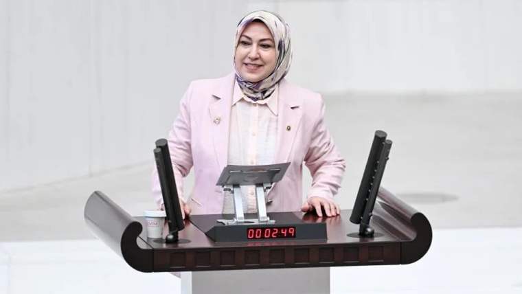 Kürsüde konuşan bir kadın, üzerinde pembe bir ceket ve başörtüsü var.