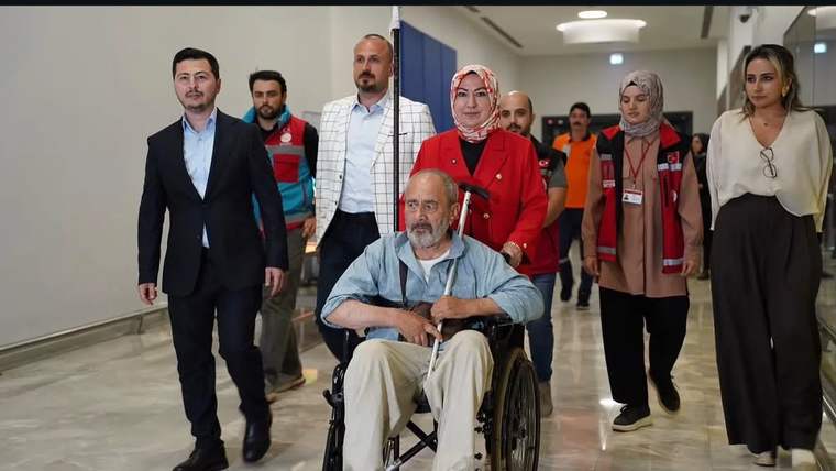 Tekerlekli sandalyede oturan bir adam, yanında yürüyen kalabalıkla birlikte bir mekandan çıkıyor.