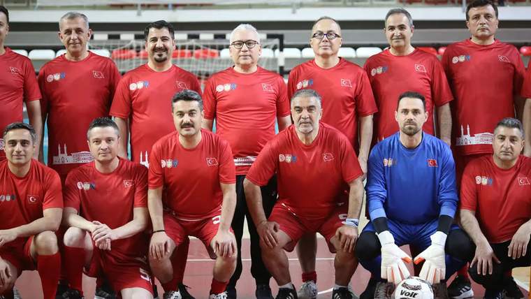 Kırmızı tişört giymiş, futbol sahasında poz veren grup, ön sırada altı kişi, arka sırada beş kişi yer alıyor.