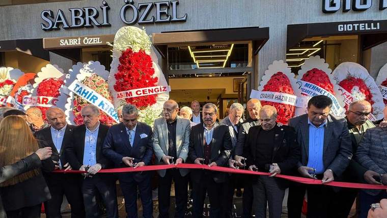 Kurdele kesen kalabalık, arka planda çiçeklerle süslenmiş dükkan girişini gösteriyor.
