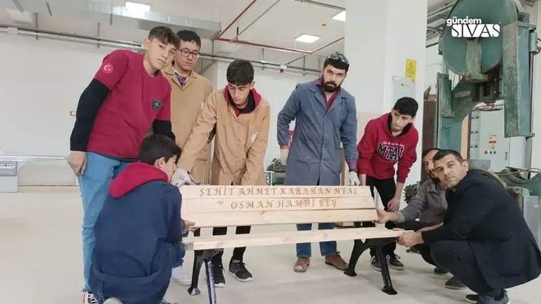Bir grup öğrenci, üzerinde yazı bulunan bir bankı montaj yaparken bir araya gelmiş.