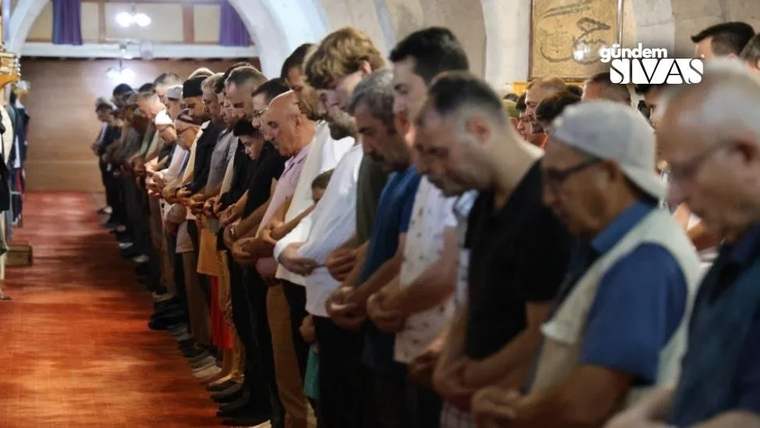 Cami içinde, namaz kılmak için diz çökerek elleriyle dua eden kalabalık bir grup insan.