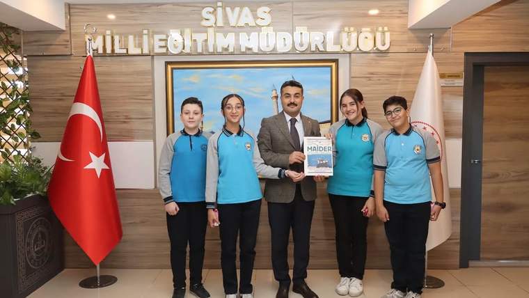 Sivas İl Milli Eğitim Müdürü ile birlikte duran dört öğrenci, MAİDER dergisini tutuyor.