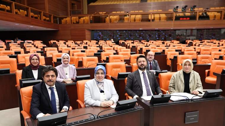 Turuncu koltuklu geniş salonda, ön sırada dört kişi ve arkalarında dört kişi oturuyor.
