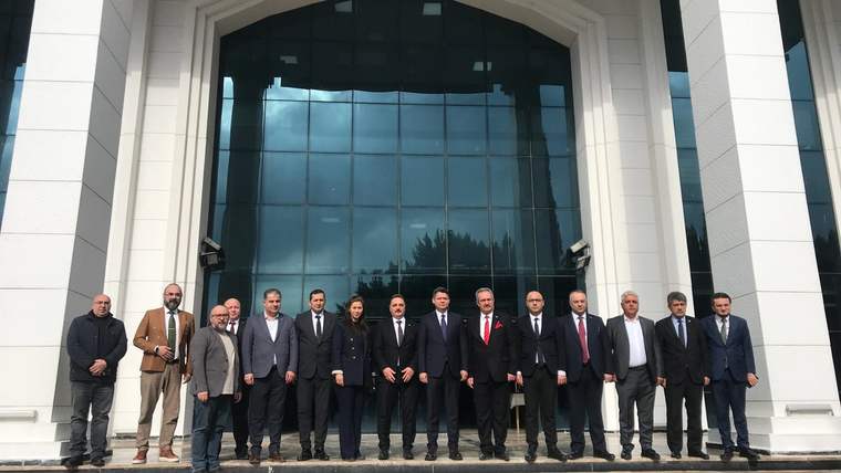 Bir grup insan, modern bir binanın önünde poz veriyor. Bina cam cepheli ve beyaz dış cepheli.