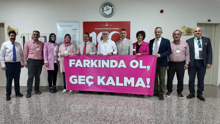 Pembe tişört giymiş bir grup insan, "FARKINDA OL, GEÇ KALMA!" yazılı büyük bir pankart tutuyor.
