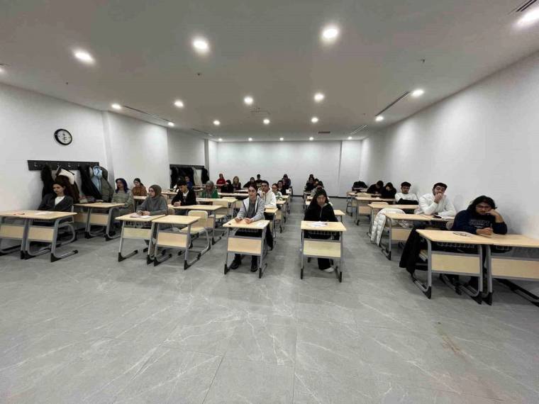 Sıralarında oturan öğrenciler, aydınlık bir sınıfta önlerindeki kâğıtlara bakıyor.