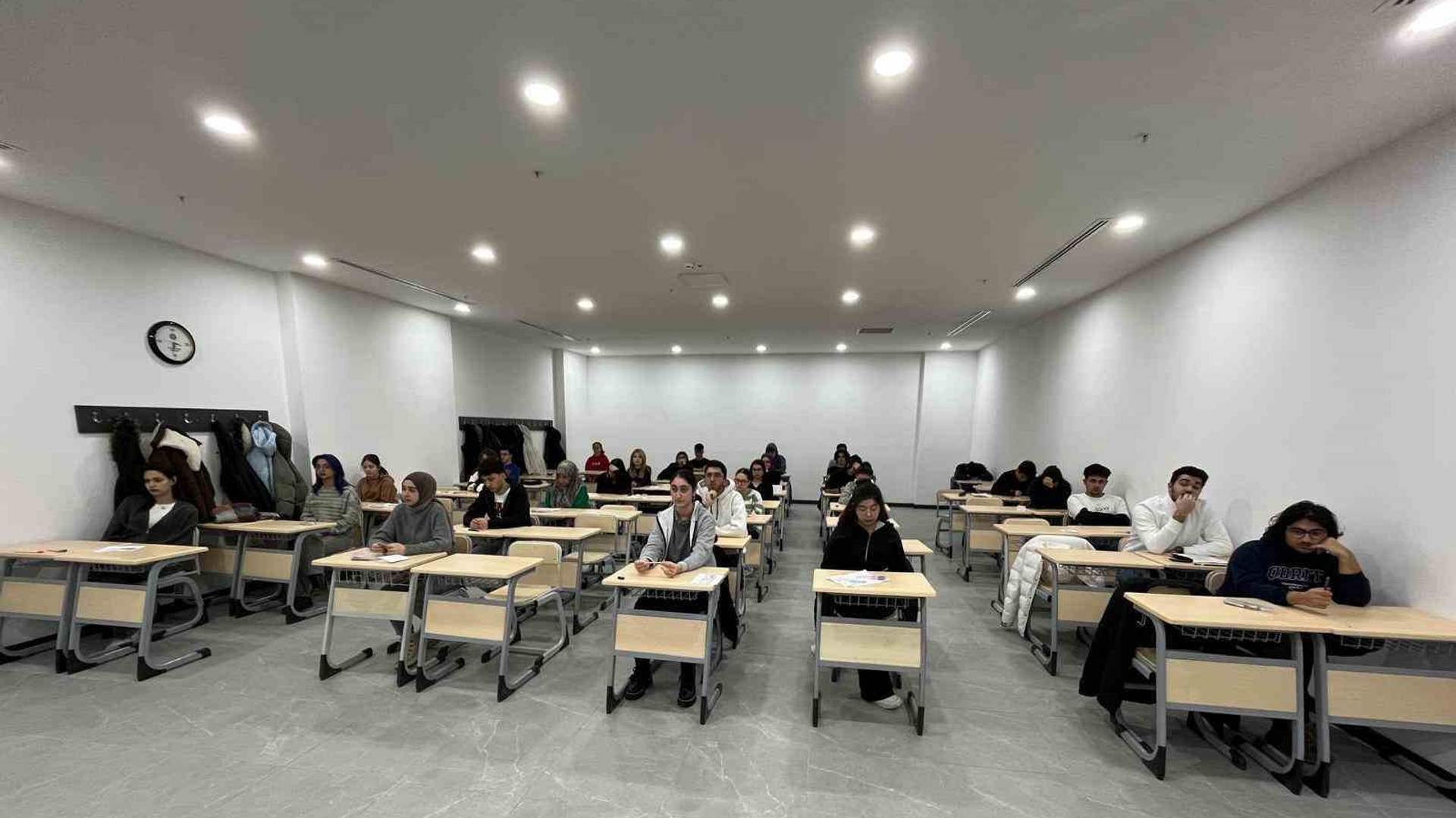 Sıralarında oturan öğrenciler, aydınlık bir sınıfta önlerindeki kâğıtlara bakıyor.