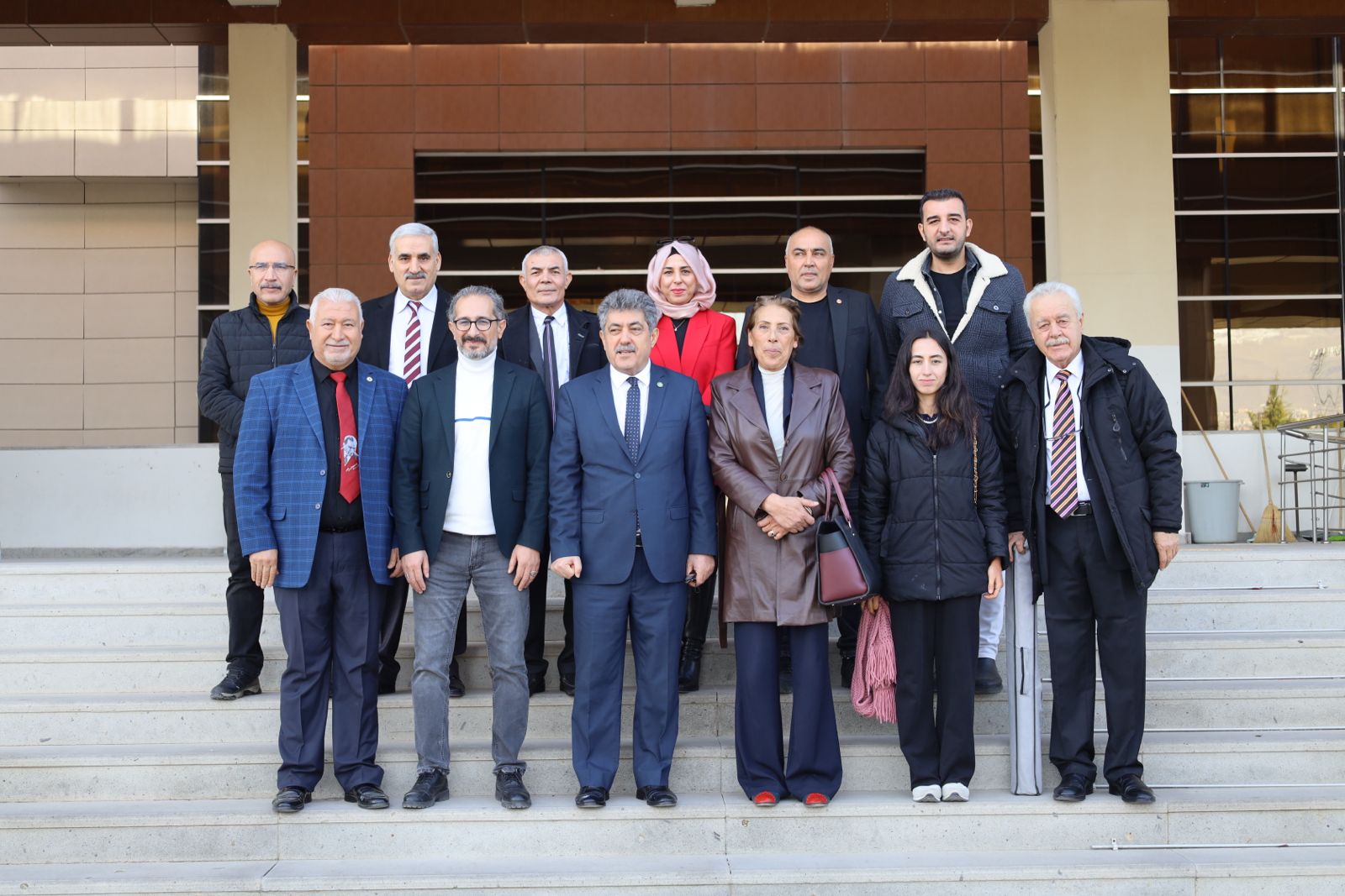 Bir grup insan, bir binanın önünde toplu halde poz veriyor.