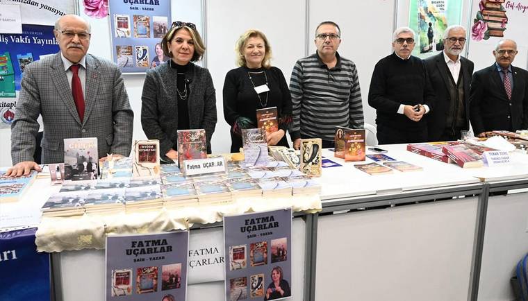 Kitaplarla dolu masanın arkasında duran yedi kişi, yayınevlerine ait afiş ve kitapların önünde poz veriyor.