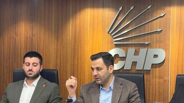 Ahşap panoda CHP logosu önünde oturan iki kişi; sağdaki kişi elini kaldırmış, soldaki kişi aşağı bakıyor.