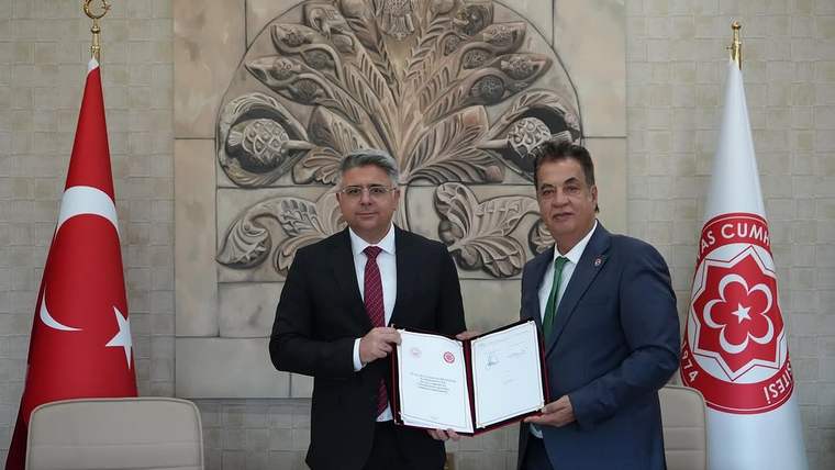 İki kişi, masada protokol belgesini tutarak poz veriyor. Arkada Türk bayrağı ve Sivas Cumhuriyet Üniversitesi logosu var.