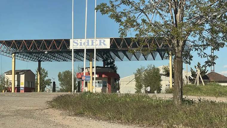 SİDEMİR fabrikasının giriş kapısı, önünde bayrak direkleri ve güvenlik kulübesi görünmekte.