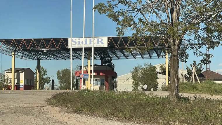 SİDEMİR fabrikasının giriş kapısı, önünde bayrak direkleri ve güvenlik kulübesi görünmekte.