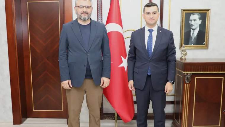 İki kişi, arka planda Türk bayrağı ve Atatürk portresi ile birlikte duruyor.