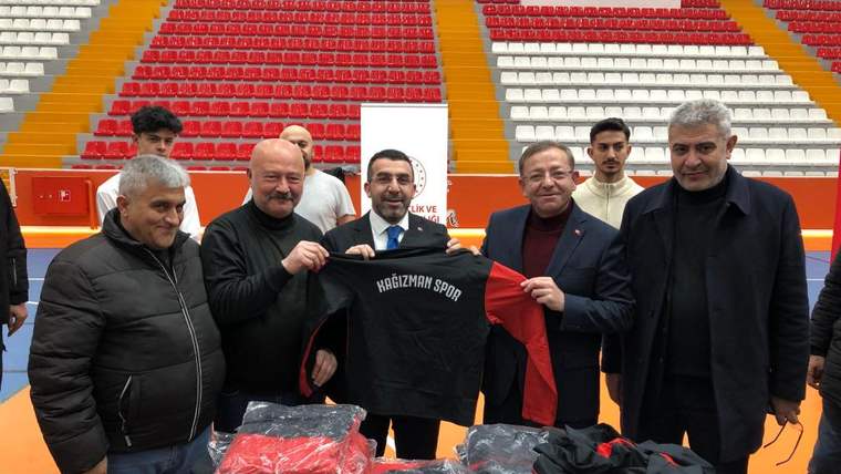 Bir grup erkek, spor malzemelerini tutarak gülümsüyor; arka planda boş tribünler var.