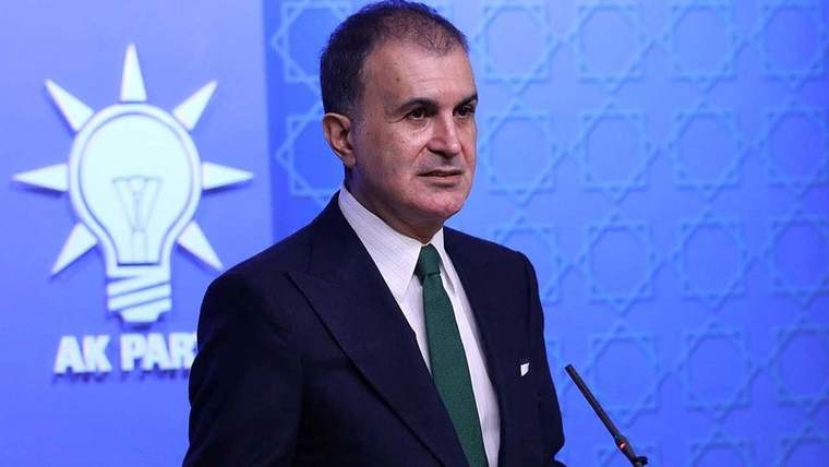 Takım elbiseli bir kişi, mavi arka plan önünde kürsü mikrofonunun yanında duruyor.
