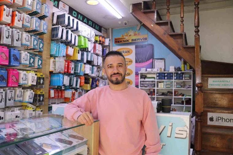 Telefon aksesuarlarıyla dolu dükkânda, cam tezgâhın arkasında pembe sweatshirtlü bir kişi duruyor.