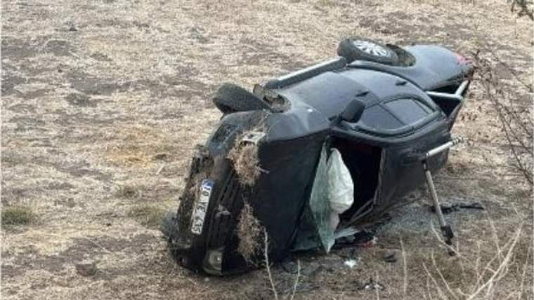 Tarlada yan yatmış otomobilin bir tekeri çıkmış, yan camı kırılmış ve içindeki hava yastığı açılmış.