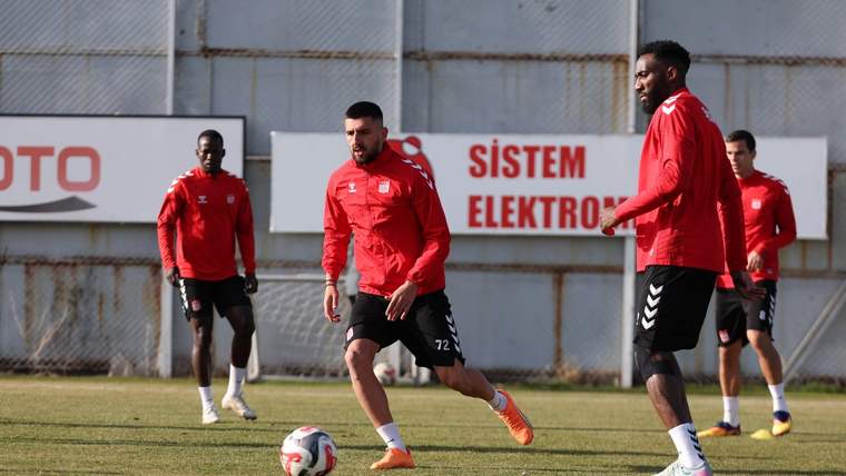 Çim sahada kırmızı formalar giyen beş futbolcu, antrenman sırasında bir topun çevresinde koşuyor.