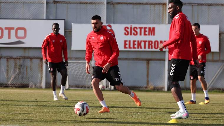 Çim sahada kırmızı formalar giyen beş futbolcu, antrenman sırasında bir topun çevresinde koşuyor.