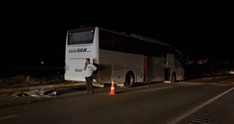 Gece yolda duran yolcu otobüsünün yanında bir kişi ve turuncu trafik konisi görülüyor.