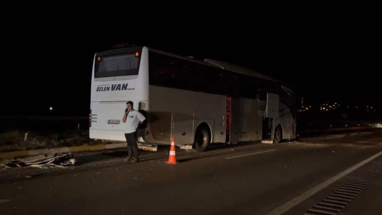 Gece yolda duran yolcu otobüsünün yanında bir kişi ve turuncu trafik konisi görülüyor.