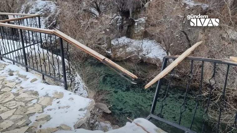 Kar kaplı taş yolun kenarındaki metal korkuluklar kırılmış; aşağıda turkuaz renkli su akıyor.