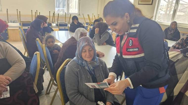 Jandarma personeli, eğitim alan bir kadına broşür gösteriyor, arka planda kadınlar oturuyor.