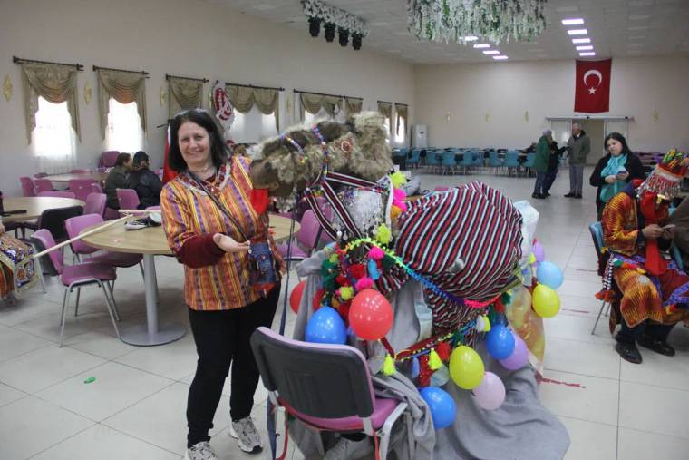 Renkli balonlarla süslenmiş bir deve, yanında geleneksel kıyafetler giymiş bir kadın duruyor.
