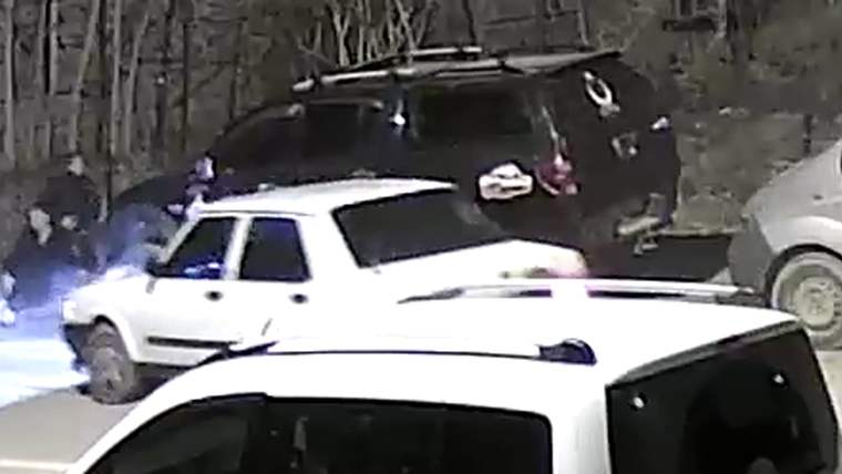 Ağaçlık alanda beyaz bir otomobil, siyah bir SUV ve kadrajın önünde başka bir araç görülüyor.
