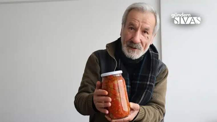 Gri saçlı ve sakallı bir erkek, içinde kırmızı yiyecek bulunan cam kavanozu iki eliyle tutuyor.