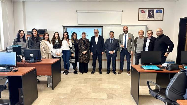 Bilgisayar sınıfında, masa ve ekranların önünde yan yana duran kadın ve erkeklerden oluşan bir grup