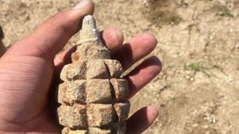 Bir kişinin elinde tutarak gösterdiği, toprak rengiyle kaplı bir el bombası.
