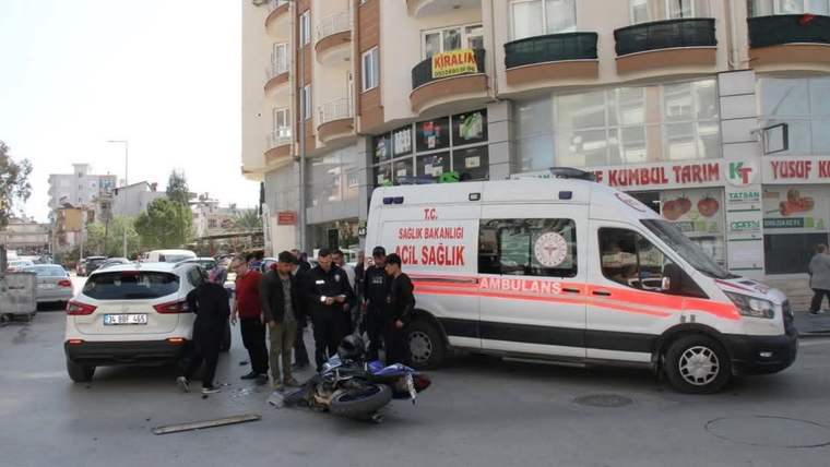 Devrilmiş motosikletin yanında toplanan kişiler ve önünde duran ambulans, şehir sokağında görülüyor.