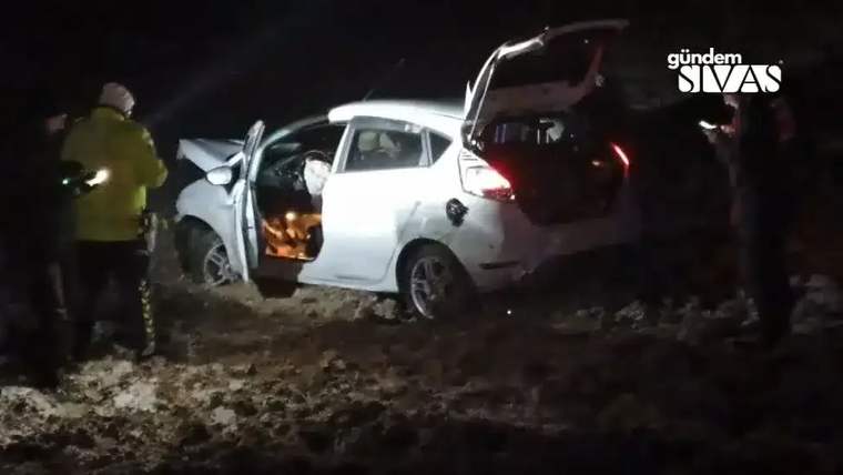 Beyaz bir otomobil, karla kaplı bir alanda yan duruyor; etrafında birkaç kişi var.