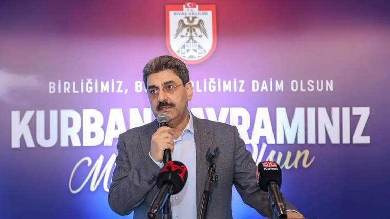 Mikrofon önünde konuşan bir kişi, arka planda Sivas Valiliği logosu ve yazılar var.