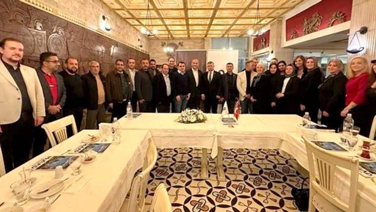 Bir grup insan, bir restoranda masanın etrafında toplanmış, fotoğraf çekiliyor.