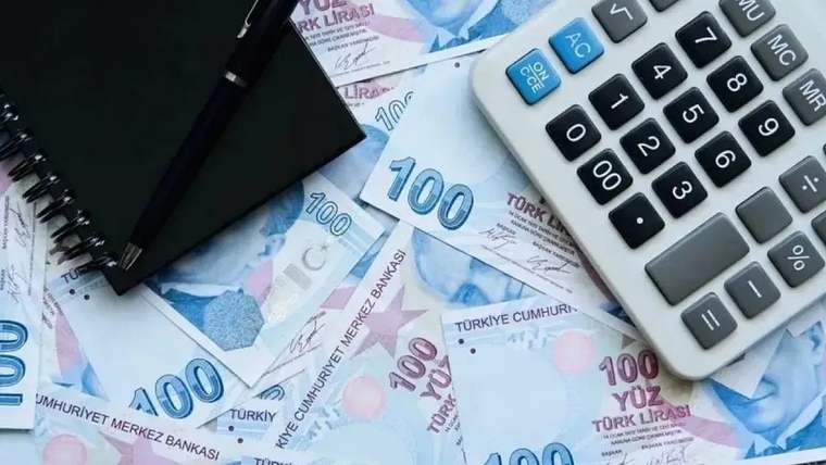 Üzerinde 100 TL banknotların yer aldığı bir masa, yanında bir hesap makinesi ve not defteri bulunuyor.