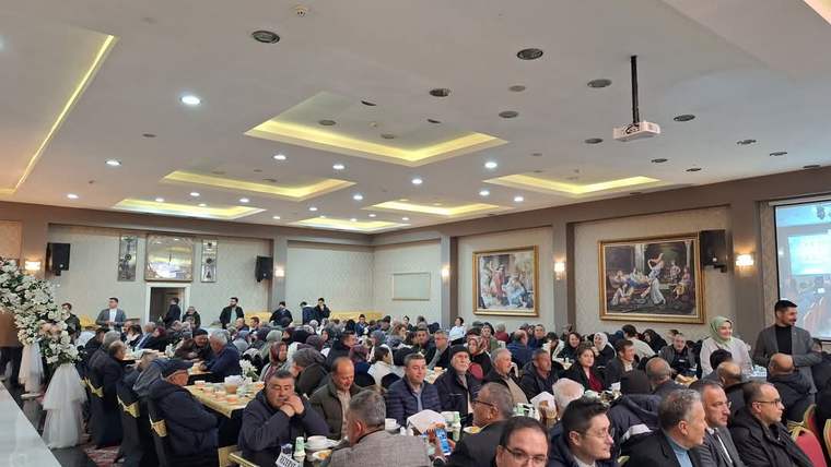 Masa ve sandalyelerle düzenlenmiş salonda çok sayıda kişi yemek yerken, duvarlarda tablolar görülüyor.