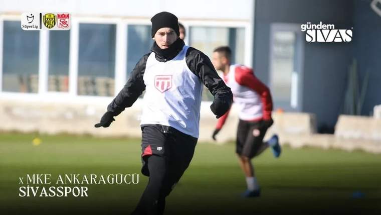Antrenman sahasında beyaz yelekli bir futbolcu koşarken, arka planda başka bir oyuncu görülüyor.