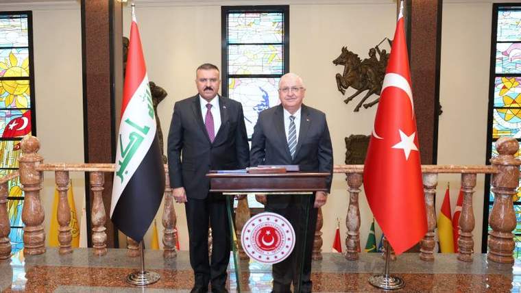 Türk ve Irak bayraklarının önünde, iki bakan yan yana duruyor.