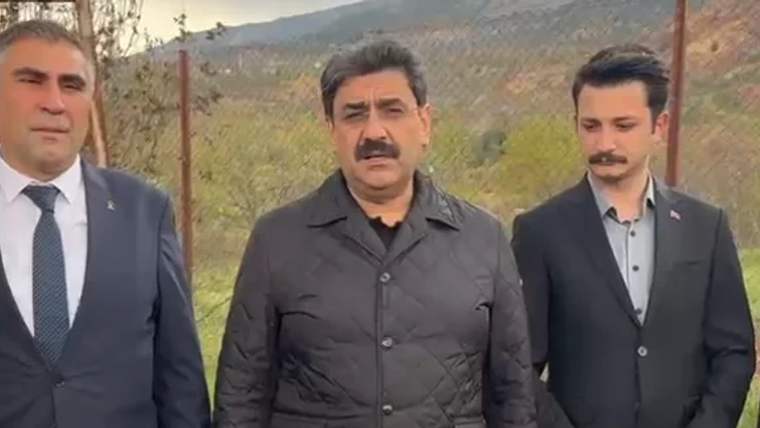 Dağlık bir arazinin önünde, ortada duran bıyıklı bir erkek ve yanında iki erkek görülüyor.