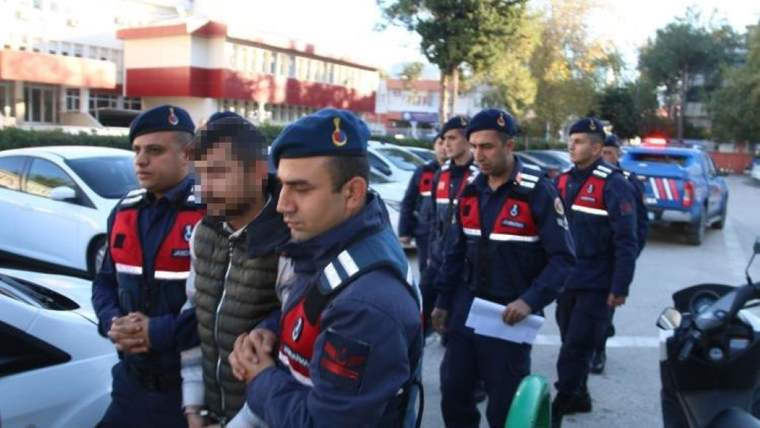 Üniformalı personel ve ortalarında duran bir kişi, park halindeki araçların yanında görülüyor.